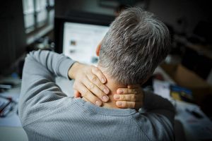 Homme de dos se tenant la nuque à cause d'une douleur aux cervicales