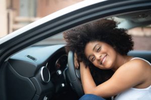 Jeune femme souriante appuyée contre le volant d'une voiture d'occasion