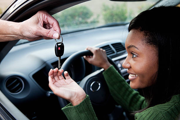 Jeune femme dans une voiture qui prend les clefs de voiture qu'on lui tend avec un grand sourire