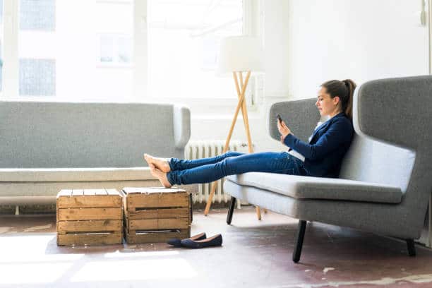 Femme assise dans son canapé avec les pieds sur sa table basse en cagettes