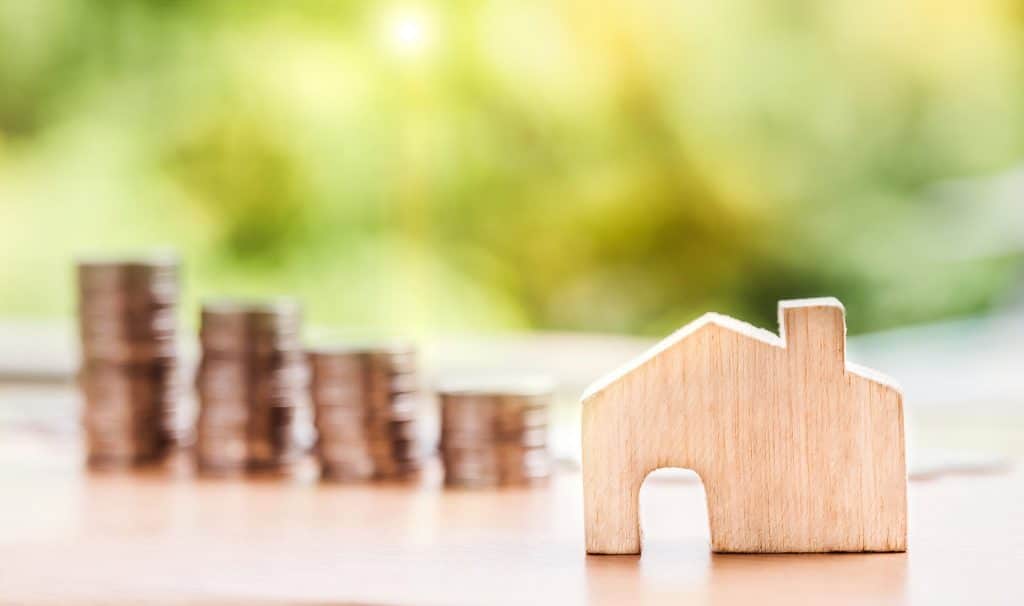 Maison miniature en bois posée sur une table avec des piles de pièces derrière